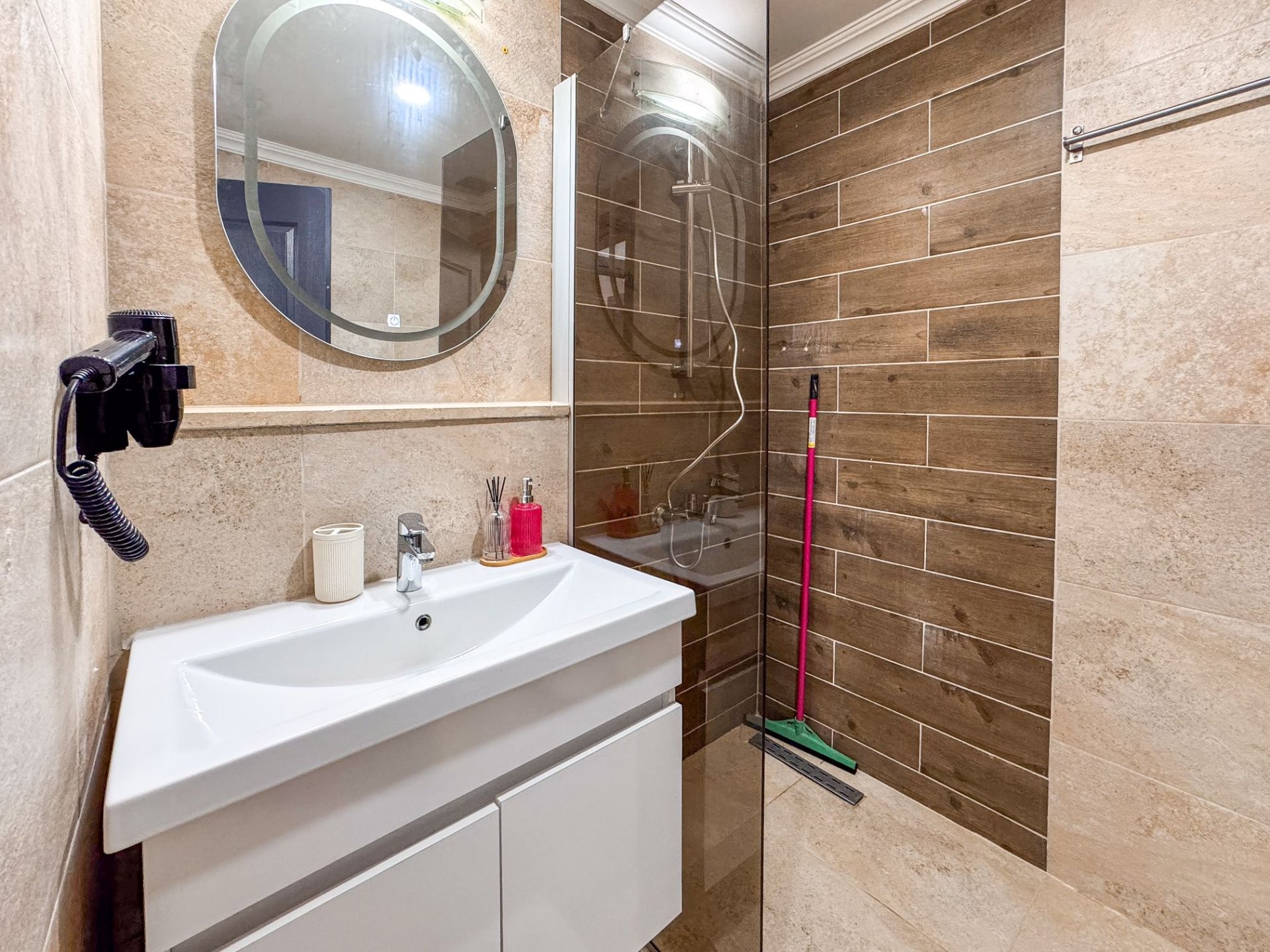 Full bathroom view with shower, vanity and warm stone-and-wood tile finishes