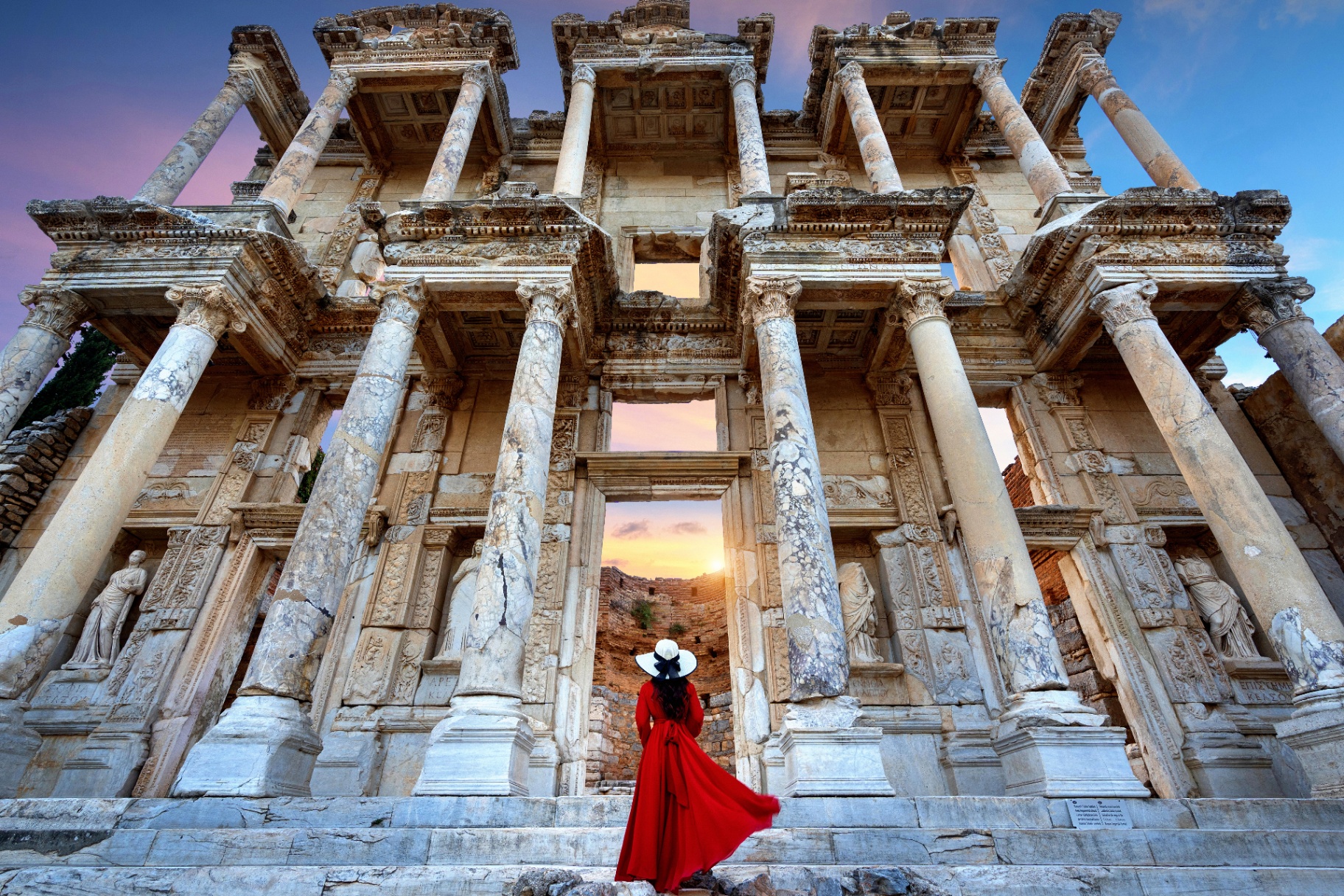 Visitor in a red dress before the marble Library of Celsus at Ephesus at sunset
