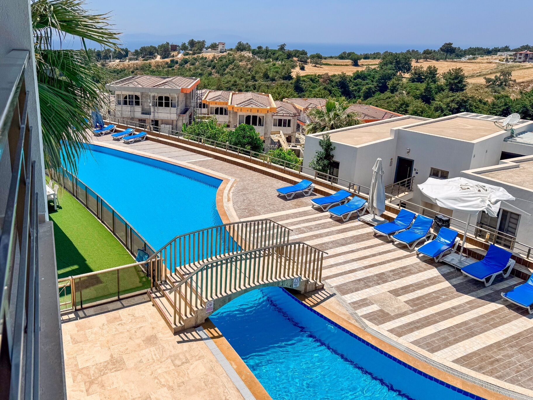 Penthouse balcony view over the curved outdoor pools, gardens and Aegean horizon