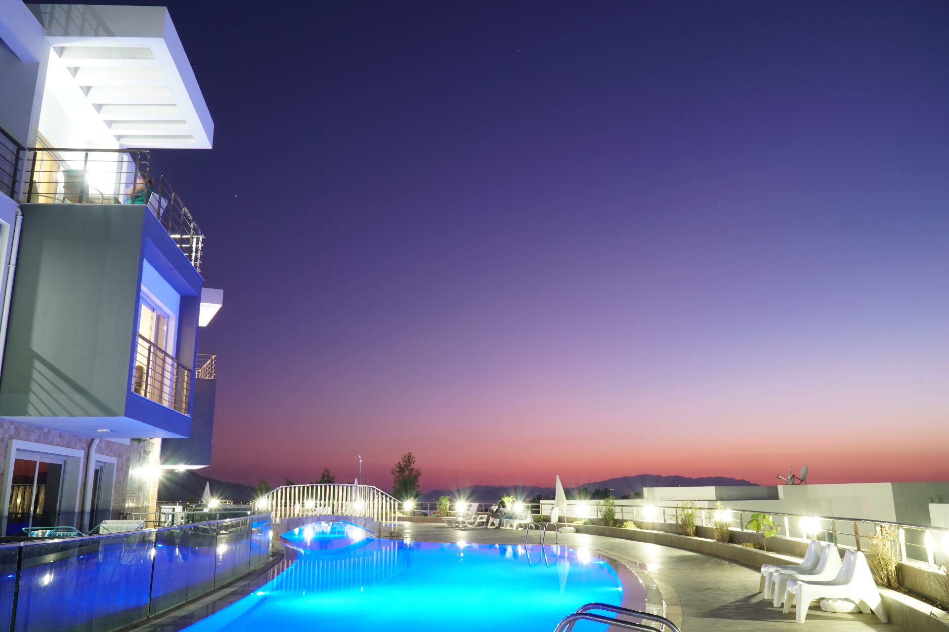 Curved illuminated swimming pool at twilight with pink and indigo sky